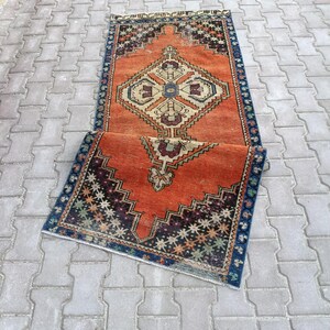 May include: Two rectangular, vintage-style rugs with intricate geometric patterns. The rugs feature a burnt orange background with dark blue, beige, and burgundy accents. The design includes diamond and zigzag motifs, creating a traditional aesthetic.