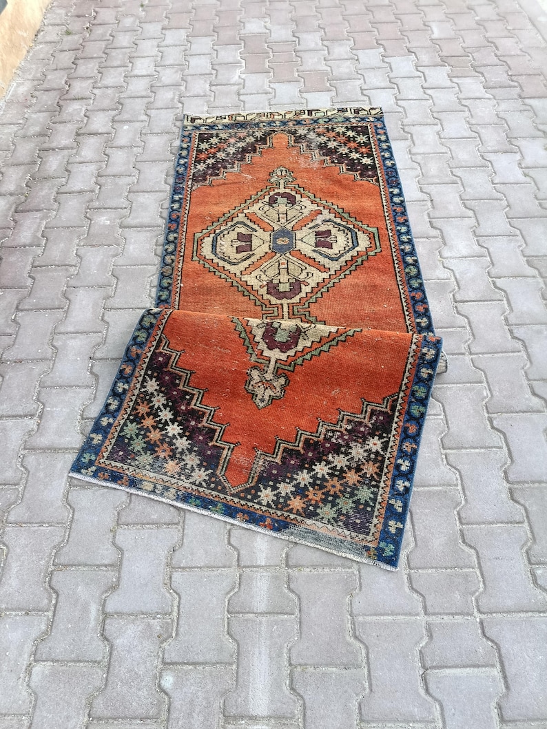 May include: Two rectangular, vintage-style rugs with intricate geometric patterns. The rugs feature a burnt orange background with dark blue, beige, and burgundy accents. The design includes diamond and zigzag motifs, creating a traditional aesthetic.
