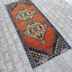 May include: A rectangular, vintage-style rug with an orange field and intricate geometric patterns. The rug features a dark blue border and decorative motifs in beige, brown, and green. The rug's dimensions are approximately 2 x 6 feet.