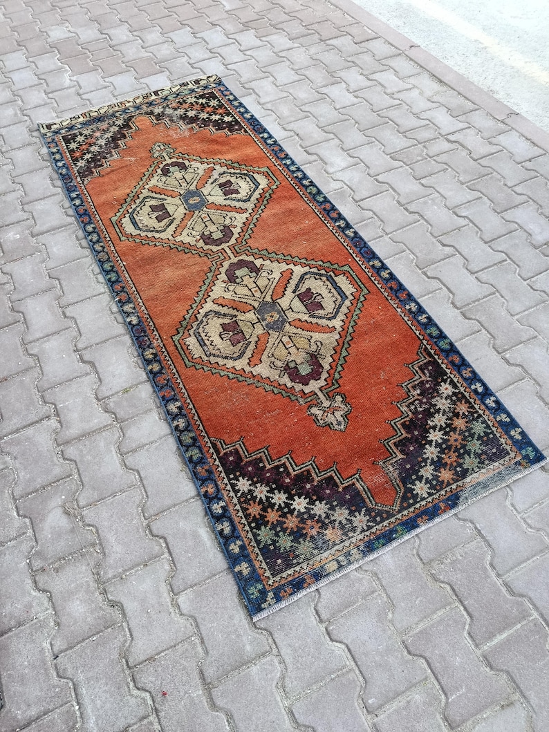 May include: A rectangular, vintage-style rug with an orange field and intricate geometric patterns. The rug features a dark blue border and decorative motifs in beige, brown, and green. The rug's dimensions are approximately 2 x 6 feet.