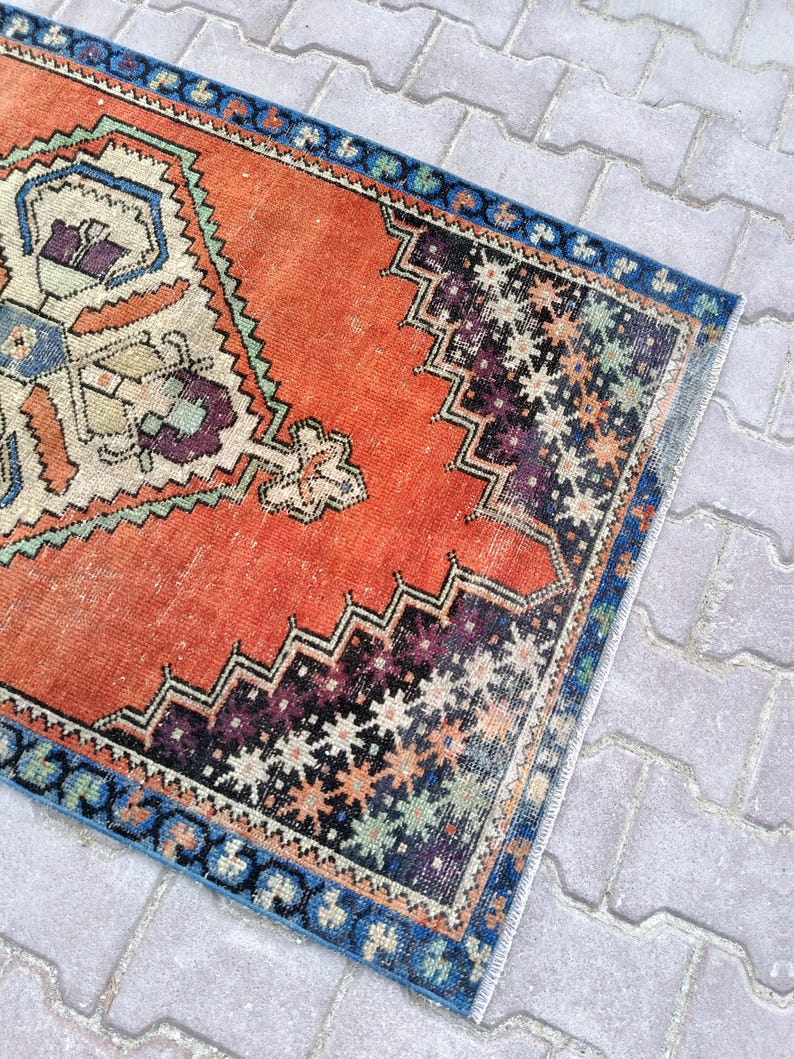 May include: A rectangular, vintage-style rug with a distressed appearance. The rug features a vibrant orange central field with intricate geometric patterns in cream, blue, purple, and black. A blue border frames the rug's edges.