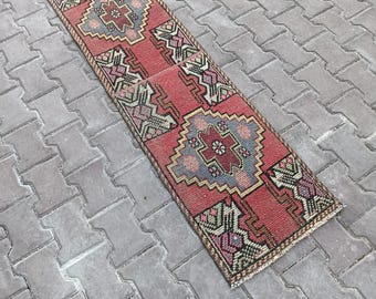 May include: A rectangular, vintage-style rug with a red background and intricate geometric patterns in shades of blue, pink, green, and beige. The rug is placed on a gray brick surface, showcasing its detailed design and texture.
