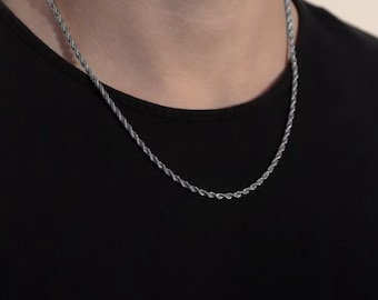 May include: A silver rope chain necklace. The necklace is worn around the neck and rests on a black top. The chain has a twisted rope design, and the metal appears to be shiny.