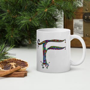 Può includere: Tazza in ceramica bianca con una lettera "F" decorativa. La lettera è adornata da un vivace mix di motivi e colori, tra cui rosso, blu, verde e giallo. La tazza ha un manico standard e una finitura lucida.