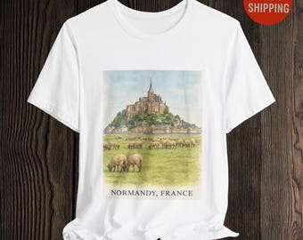 May include: White t-shirt with a watercolour illustration of a castle on a hill and sheep grazing in a field. The text "NORMANDY, FRANCE" is below the image. A red circle with the words "FAST SHIPPING" is in the upper right corner.