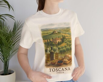 May include: Cream-colored t-shirt featuring a scenic Tuscan landscape with olive trees, rolling hills, and a villa. The image includes olive oil bottles, olives, and bread. The text "Toscana Italia" is printed at the bottom.