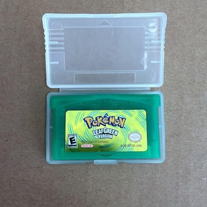 Könnte beinhalten: Eine grüne Pokémon LeafGreen Version Game Boy Advance-Cartridge in einer transparenten Kunststoffhülle. Die Cartridge hat ein gelbes Etikett mit dem Pokémon-Logo und dem Spieletitel. Die Hülle ist geöffnet und zeigt die Spielcartridge.