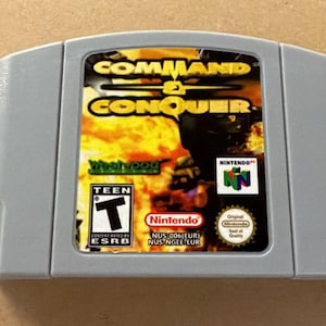 Może przedstawiać: Szary kartridż z grą wideo na konsolę Nintendo 64, Command & Conquer. Etykieta przedstawia ogniste tło, tytuł gry żółtą czcionką, klasyfikację wiekową ESRB Teen, logo Nintendo 64, logo Westwood Studios oraz pieczęć jakości Nintendo.