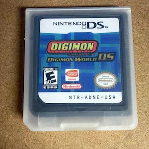 Puede incluir: Un cartucho de juego negro de Nintendo DS para Digimon World DS, alojado en una funda de plástico translúcido. La etiqueta muestra el título del juego, el logotipo de Bandai Namco, una clasificación ESRB Everyone 10+, el sello oficial de Nintendo y el código NTR-ADNE-USA.