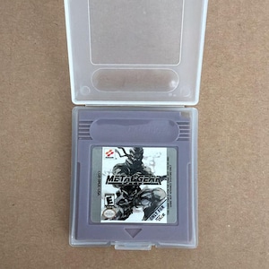 May include: A purple Metal Gear Solid video game cartridge for the Game Boy Color, in a clear plastic case. The cartridge has the game title and a graphic of a character. The case is open.