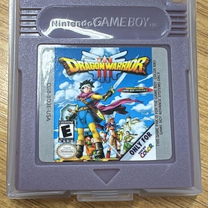 以下が含まれることがあります： 透明なプラスチックケースに入った、紫色のNintendo Game Boy用ドラゴンクエストIIIのゲームカートリッジ。ゲームのラベルには、剣を持ったキャラクターが描かれた青色の背景があります。