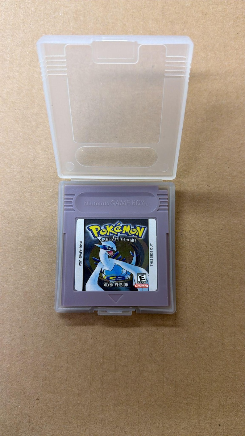 May include: A purple Nintendo Game Boy cartridge for the game "Pok&eacute;mon Silver Version" is displayed inside a clear plastic case. The cartridge has the Pok&eacute;mon logo and the text "Gotta catch 'em all!"