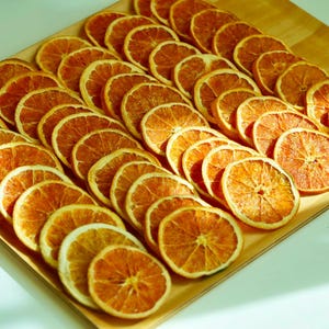 May include: A wooden tray filled with numerous dried orange slices. The slices are arranged in neat rows, showcasing their vibrant orange color and textured surfaces. The image is well-lit, highlighting the details of the fruit.