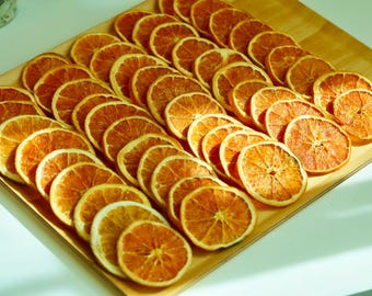 May include: A wooden tray filled with numerous dried orange slices. The slices are arranged in neat rows, showcasing their vibrant orange color and textured surfaces. The image is well-lit, highlighting the details of the fruit.