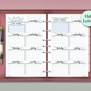 May include: A pink leather planner with a weekly layout, featuring sections for each day, labeled Monday through Sunday. The planner includes a "Top Three" section and a "Don't Forget" section. A decorative pen rests on the side.