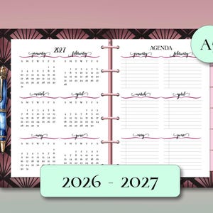 May include: An open A5 planner with a pink spine, featuring calendar pages for 2027 and agenda pages. The cover has a dark geometric design. A pen with blue and gold accents rests on the left page. The text "2026 - 2027" is at the bottom.
