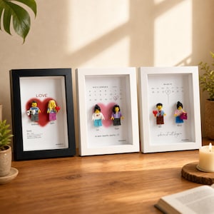 May include: Three rectangular shadow box frames containing custom displays. One black frame features a red heart and two minifigures labeled Andrew and Beth. Two white frames feature calendar dates, red hearts, and pairs of minifigures labeled with names.