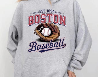 May include: A light gray hoodie featuring a baseball design. The design includes the text "EST. 1894 BOSTON Baseball" in red and blue, with a baseball and mitt graphic. The hoodie has a drawstring hood and a front pocket.