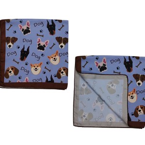 May include: Two blue dog-themed blankets with a brown border. The blankets feature various dog breeds, bones, paw prints, and the word "Dog" in white. One blanket is folded, revealing the underside with a similar pattern.