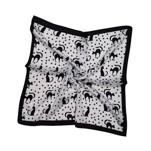 May include: Square white scarf with a black border, featuring a pattern of black cat silhouettes and small black polka dots. The scarf is folded and twisted, showcasing the design.
