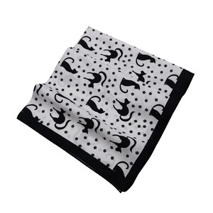 May include: White square scarf with a black border and a repeating pattern of black cat silhouettes and small black paw prints. The scarf is folded and appears to be made of a lightweight fabric.