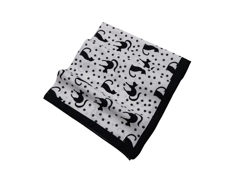 May include: White square scarf with a black border and a repeating pattern of black cat silhouettes and small black paw prints. The scarf is folded and appears to be made of a lightweight fabric.