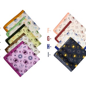 May include: Nine colorful handkerchiefs with celestial eye, moon, and star patterns. Each handkerchief has a different border color, including gold, green, brown, purple, peach, and navy. The handkerchiefs are arranged in a fan shape.
