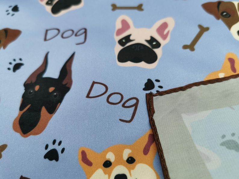 May include: Light blue fabric with repeating dog-themed illustrations. Features various dog breeds, paw prints, and the word "Dog" in brown. A portion of a light blue and brown-edged square is visible.