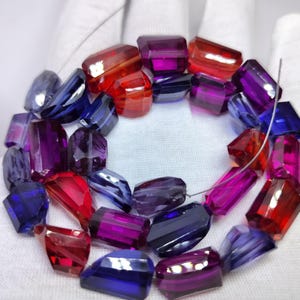 May include: A collection of faceted, translucent beads in vibrant shades of red, purple, and blue, strung together on a thin wire. Each bead features a polished, irregular geometric shape that reflects light, creating a multi-coloured display.