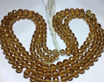 May include: A strand of faceted, amber-colored beads. The beads are strung together, forming multiple loops. A white tassel is attached to the end of the strand. The beads have a sparkling, polished appearance.