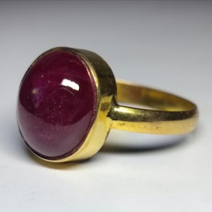 Op de afbeelding: Een gouden ring met een grote, ovaal geslepen robijn. De robijn heeft een diepe, rijke rode kleur en is gezet in een gouden band. De ring heeft een klassiek, elegant ontwerp.