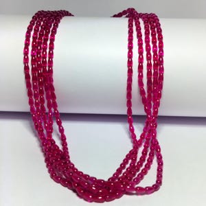 May include: A multi-strand necklace featuring numerous small, translucent, deep pink beads shaped like elongated ovals. The beads are strung together in several long, flowing strands that drape downward, creating a layered effect with a vibrant color.