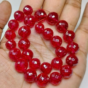 May include: A strand of round, faceted, translucent red beads. Each bead features a geometric cut surface that reflects light, creating a sparkling appearance. The beads are strung together on a thin, flexible wire, forming a circular arrangement.