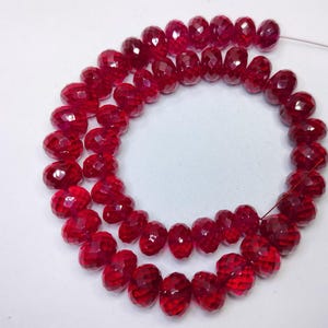 May include: A strand of vibrant red, faceted, circular beads arranged in a loose spiral. Each bead features a polished, multi-faceted surface that reflects light, creating a sparkling appearance. The beads are strung together on a thin, metallic wire.