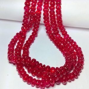May include: Strands of vibrant red gemstone beads. The beads are small, round, and strung together, creating a flowing, textured appearance. The color is a deep, rich red, with a slight translucence.