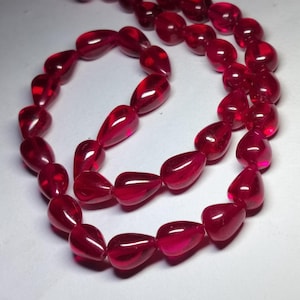 May include: A necklace of translucent, teardrop-shaped beads in a deep red hue. The beads are strung together, creating a flowing, elegant design. The glossy finish of the beads reflects light, enhancing their rich color and visual appeal. This jewelry piece is suitable for various occasions.