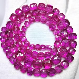Pode incluir: Um fio de contas de pedras preciosas em rosa fúcsia vibrante dispostas num padrão circular. Cada conta apresenta uma forma de almofada facetada que reflete a luz, criando um aspeto cintilante em toda a coleção de pedras translúcidas.