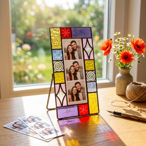 May include: A rectangular stained glass photo frame with a multi-coloured border of yellow, purple, and pink geometric tiles. The frame holds a vertical strip of three photographs featuring a couple. A metal stand supports the frame upright.