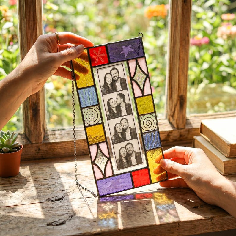 May include: A rectangular stained glass photo frame featuring a central vertical strip of four black and white portrait photos. The border is composed of multi-colored glass pieces in red, yellow, blue, purple, and pink with geometric patterns.