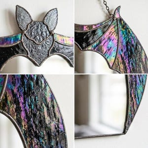 May include: A stained glass bat suncatcher featuring iridescent black and purple textured glass panels held together by dark metal solder lines. The bat has pointed ears and outstretched wings, with a metal chain attached for hanging display.