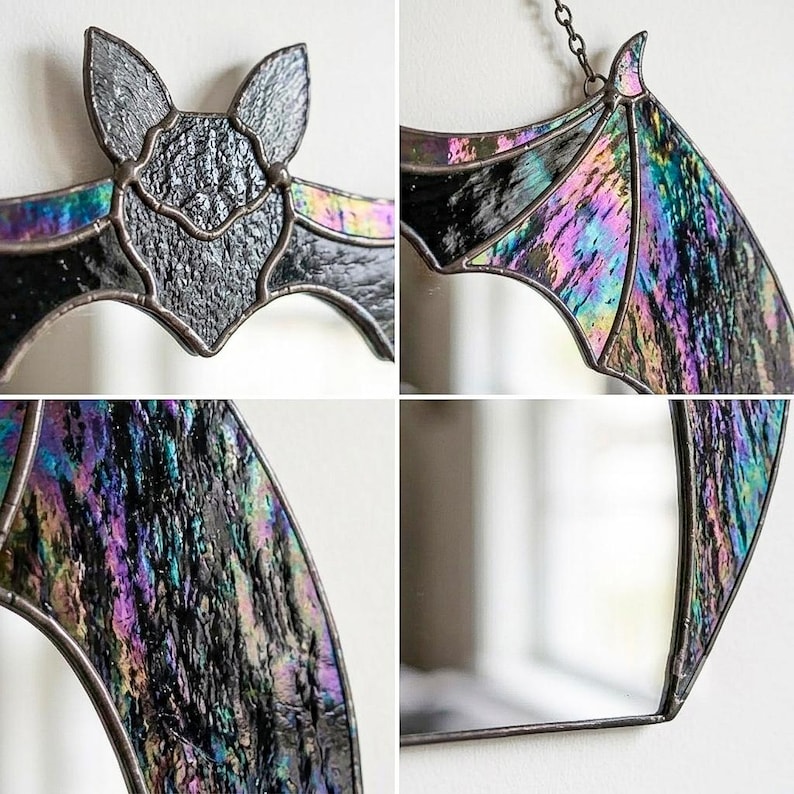 May include: A stained glass bat suncatcher featuring iridescent black and purple textured glass panels held together by dark metal solder lines. The bat has pointed ears and outstretched wings, with a metal chain attached for hanging display.