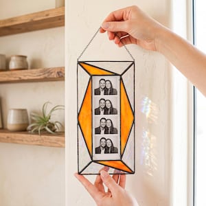 May include: A rectangular stained glass photo frame featuring a central vertical strip holding a black and white photo booth strip of a couple. The frame has orange and iridescent white glass panels held together by dark metal solder lines.