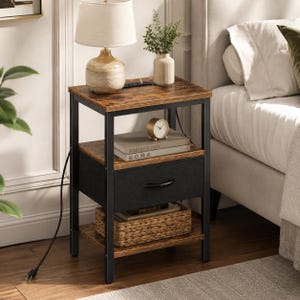 May include: A rustic nightstand with a brown wood-look top and shelves, supported by a black metal frame. It features a black drawer, a woven basket, and a small gold-colored clock. A lamp and a vase with greenery sit on top.