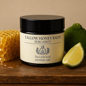 Könnte beinhalten: Ein schwarzes Glas Tallow Honey Balm mit einem cremefarbenen Etikett, auf dem das Wort "Bergamotte" steht. Eine Honigwabe, eine Limette und ein Limettenschnitz liegen neben dem Glas. Auf dem Etikett steht auch "The Little Leaf Apothecary".