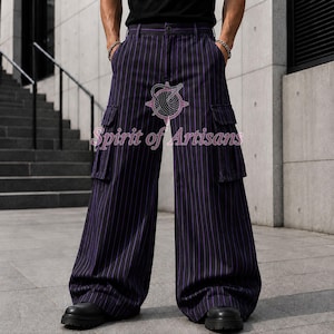 May include: Wide-leg cargo pants in a dark navy blue fabric with vertical purple pinstripes. The pants feature two large side cargo pockets with flaps, a button closure at the waist, and belt loops. The text Spirit of Artisans is visible.