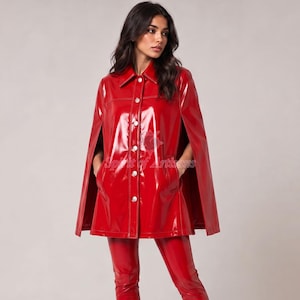 May include: A glossy red vinyl cape jacket featuring a classic collar, a front button-down closure with silver-toned buttons, and open arm slits. The garment has a smooth, reflective finish and is paired with matching red vinyl trousers.