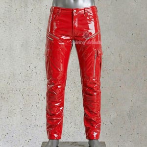 Puede incluir: Pantalones rojos brillantes con múltiples bolsillos y cremalleras plateadas. Los pantalones tienen un acabado brillante y un emblema decorativo cerca del bolsillo derecho. Los pantalones se exhiben en un maniquí.