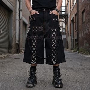 May include: Black denim shorts featuring red contrast stitching, silver-tone metal eyelets, and decorative chain lacing down the front panels. The shorts include multiple pockets, metal D-rings, and a detachable chain strap hanging from the waist.