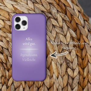 May include: A lilac phone case featuring the German text "Alles wird gut. Irgendwann. Vielleicht." The case is displayed on a woven surface. The text "Available for iPhone and Samsung" is also visible.