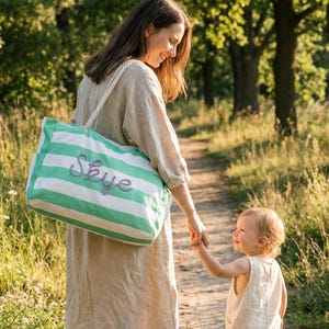 Mother and child walking in a park, mom is wearing a custom green striped canvas tote bag with zipper, a great personalized Mother's Day gift for mom